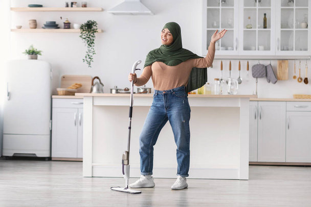Porträt einer fröhlichen muslimischen Frau, die singend Boden putzt und einen Wischmopp hält - Foto, Bild