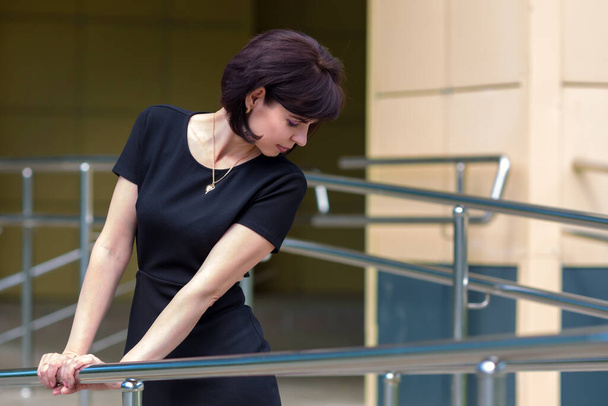 slender brunette in a black dress with slits at waist comes out of the bank. - Foto, Imagen