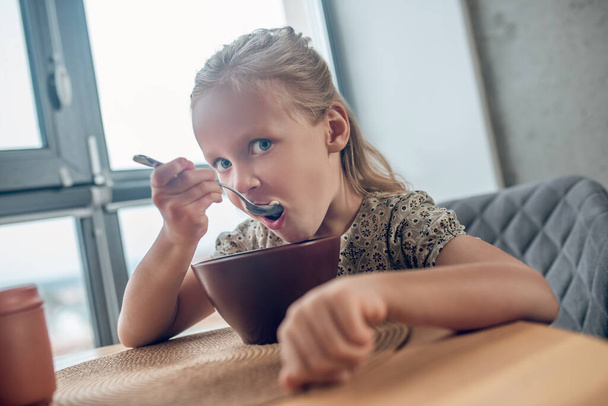 A cute blone girl eating her breakfast and looking involved - Fotoğraf, Görsel