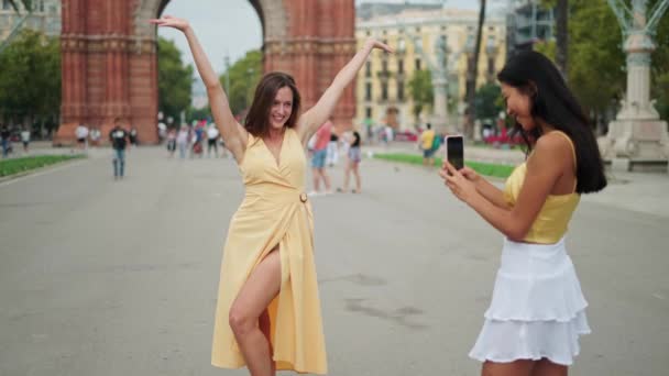 Jeune femme touriste posant pour la photo contre arc de triomphe tandis que son amie femme faisant des photos - Séquence, vidéo