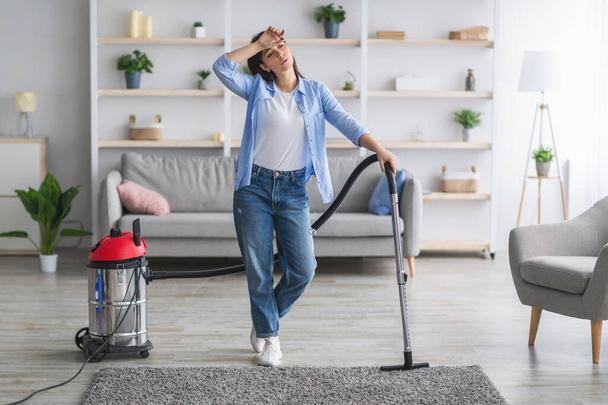 Втомлена жінка прибирає підлогу з пилососом у вітальні
 - Фото, зображення