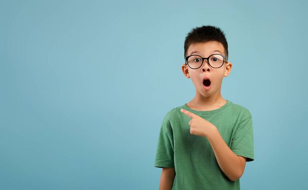Удивительное предложение. Возбужденный азиатский мальчик в очках, указывающий на копировальное пространство - Фото, изображение