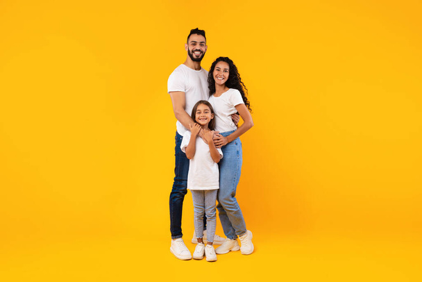 Ganzkörperaufnahme einer nahöstlichen Familie, die sich auf gelbem Hintergrund umarmt - Foto, Bild