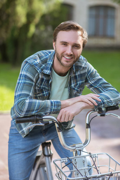 A smiling man in a plaid shirt on a bike - Фото, изображение