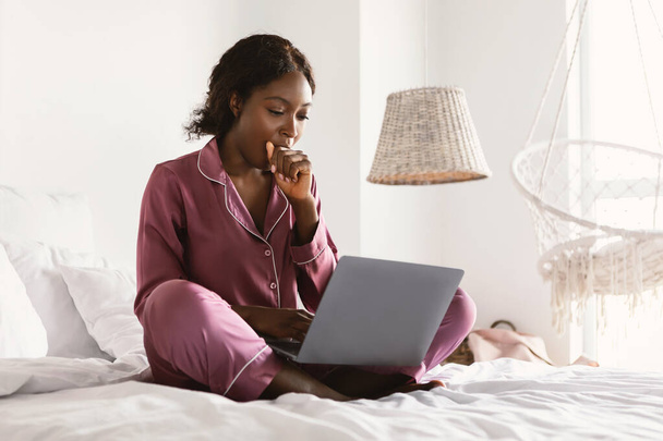 ベッドルームでノートパソコンとヨーニングを使用して眠そうなアフリカのフリーランサー女性 - 写真・画像