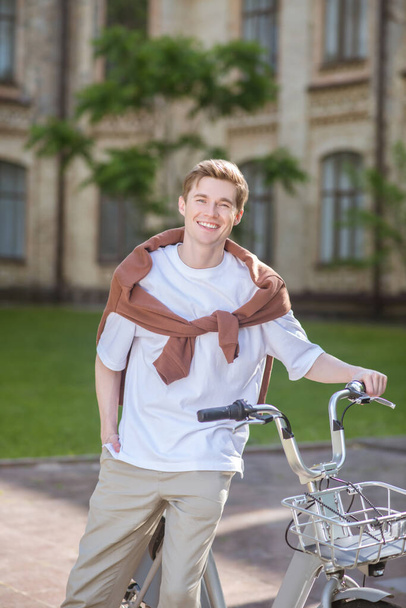 Una foto de un joven parado cerca de la bicicleta - Foto, Imagen