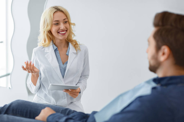 Χαμογελαστή οδοντίατρος γυναίκα έχει συνομιλία με τον ασθενή αρσενικό - Φωτογραφία, εικόνα