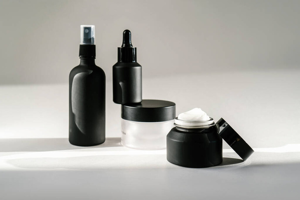 Black cosmetic bottles on a background flooded with sunlight. - Valokuva, kuva