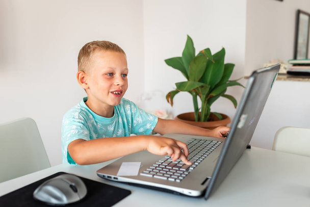 Little young school boy working at home with a laptop and class notes studying in a virtual class having video conference on laptop with teacher from home. Distance education and learning, e-learning, online learning concept during quarantine - Fotó, kép