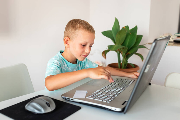 Little young school boy working at home with a laptop and class notes studying in a virtual class having video conference on laptop with teacher from home. Distance education and learning, e-learning, online learning concept during quarantine - Foto, Imagem