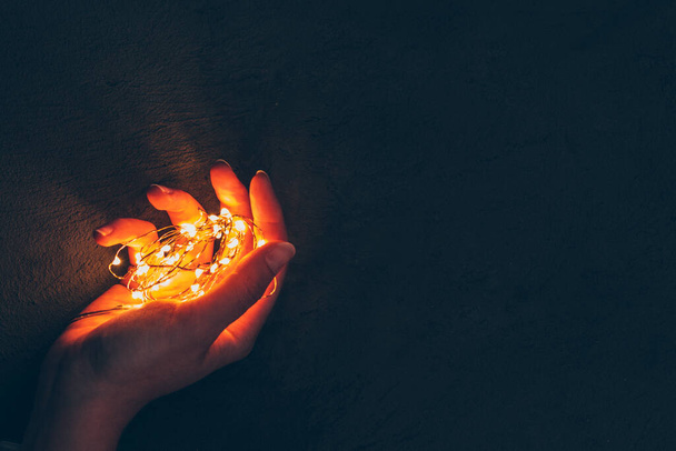 Woman hand holding illuminated garland in her hands in dark - Foto, Imagem