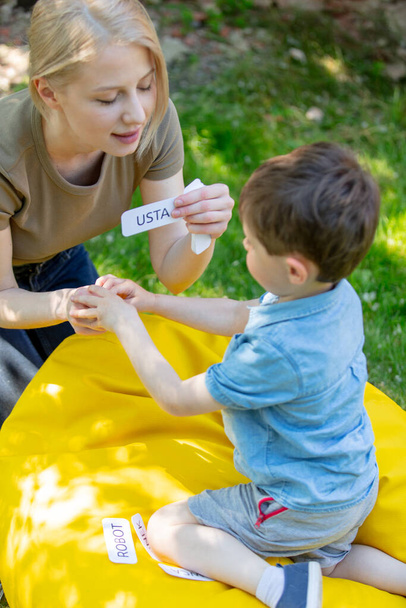 mom διδάσκει να προφέρει λέξεις χρησιμοποιώντας την τεχνική Doman για ένα αυτιστικό παιδί στην αυλή - Φωτογραφία, εικόνα