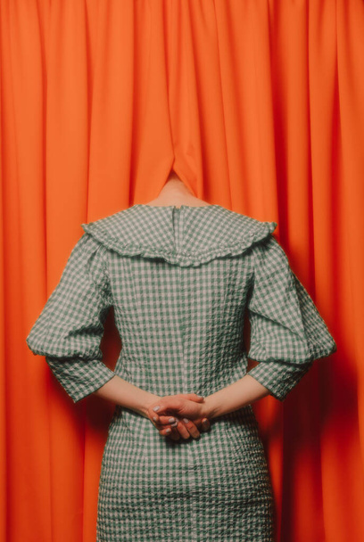 κορίτσι σε ένα πράσινο φόρεμα κρύβει το κεφάλι της σε πορτοκαλί κουρτίνες  - Φωτογραφία, εικόνα