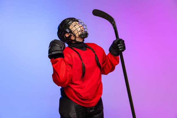 Portret van een professionele hockeyspeelster in een speciale beschermhelm, geïsoleerd over een helderblauwe paarse achtergrond. Hoge motivatie - Foto, afbeelding