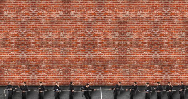 Team competing in tug of war. While some strive and do their duty, others are inattentive and delegate the work to others. Background of red bricks wall - Photo, Image