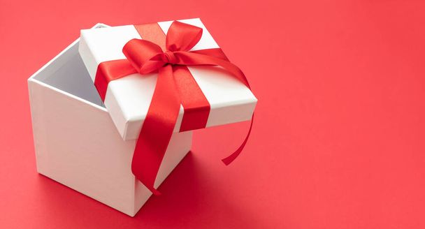 Kerstcadeau doos wit met rood lint strik open op rode achtergrond, Valentijnsdag verrassing, Nieuwjaar vakantie cadeau, satijn krullend decoratie. Kopieerruimte, wenskaart sjabloon - Foto, afbeelding