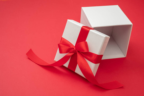 Christmas gift box white with red ribbon bow open on red color background, Valentine surprise, New Year holiday present, satin curly decoration. Copy space, greeting card template - Photo, Image