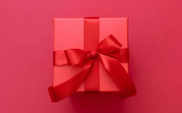 Kerst rood geschenkdoos gebonden strik met lint op rode achtergrond, Valentijnsdag verrassing, Nieuwjaar vakantiegeschenk, satijnen krullende decoratie, bovenaanzicht. - Foto, afbeelding