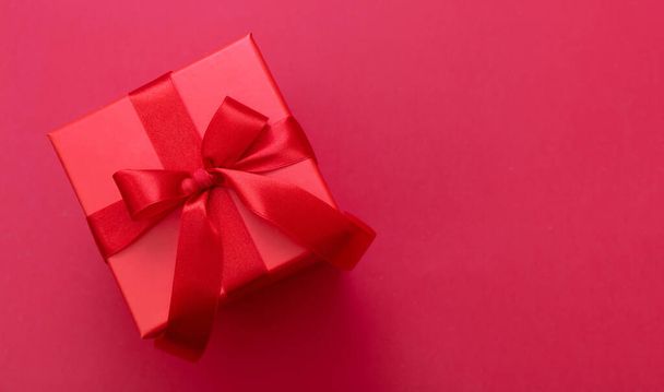Karácsonyi piros ajándék doboz kötött íj szalag piros színű háttér, Valentin meglepetés, szilveszter ajándék, szatén göndör dekoráció, felső nézet. Fénymásolási hely, üdvözlőkártya sablon - Fotó, kép