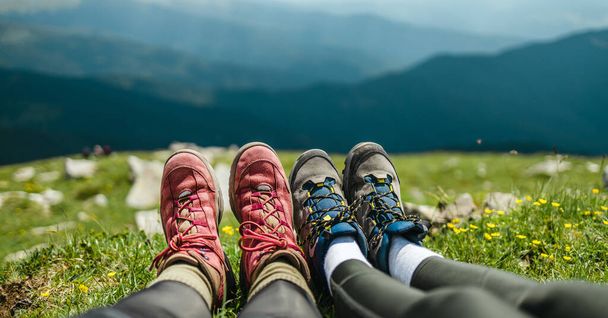 Mladý pár táboří v horách. Pěší túry v trekingových botách relaxují po dlouhé túře na vrcholu kopce za slunečného dne. Dovolená a cestování. Úžasné karpatské horské panorama - Fotografie, Obrázek