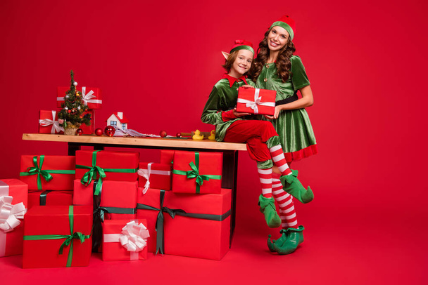 Full length body size view of two attractive cheerful friends elf holding craft giftboxes hugging isolated over bright red color background - Photo, Image