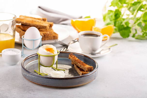 Вкусный завтрак с мягкими варёными яйцами, жареным хлебом, чашкой кофе и апельсиновым соком. - Фото, изображение