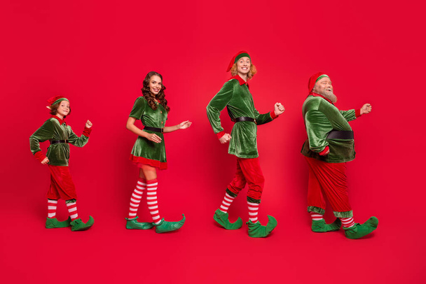 Full body photo of happy santa helper walk go empty space xmas mood wear hat isolated on red color background - 写真・画像