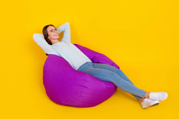 Full body photo of happy dream woman enjoy sit bean bad hands behind head empty space look isolated on yellow color background - Foto, Imagen