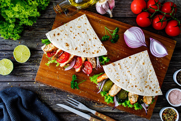 Italian piada wraps - piadina stuffed with fresh vegetables and roast chicken breast on wooden table  - Foto, imagen