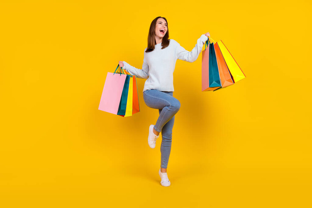Full length photo of happy young woman hold hands bags look empty space win sale isolated on yellow color background - Fotografie, Obrázek