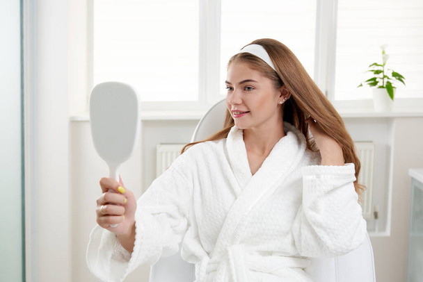 Mujer en el salón de cosmetología satisfecho con el resultado del procedimiento cosmético. Mujer mirando el espejo y examinando la piel - Foto, Imagen