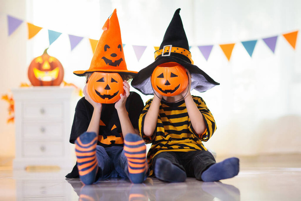 Little girl and boy in witch costume on Halloween trick or treat. Kids holding candy in pumpkin lantern bucket. Children celebrate Halloween at decorated fireplace. Family trick or treating. - Fotografie, Obrázek