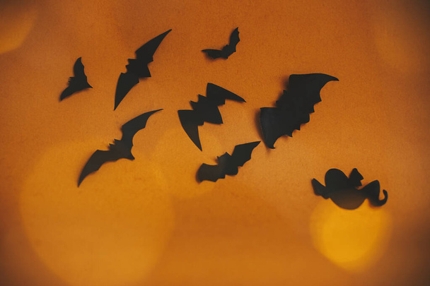 Halloween background. Bats flying on dark orange background with magical lights bokeh. Happy Halloween. Atmospheric mood. Greeting card with space for text. Festive evil spooky decorations - Photo, Image