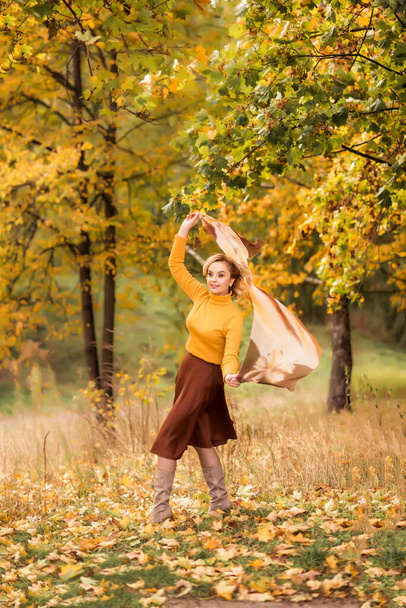 Una anciana está girando en un parque de otoño sobre un fondo de hojas amarillas. Disfrutando de la vida. - Foto, imagen