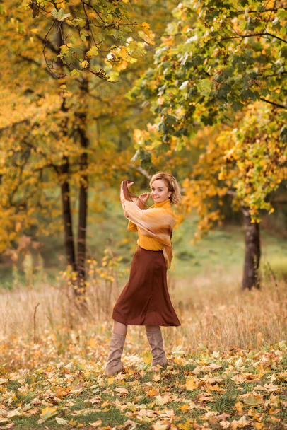 Yaşlı bir kadın, bir sonbahar parkında sarı yapraklardan oluşan bir arka plana doğru dönüyor. Hayatın tadını çıkarıyorum.. - Fotoğraf, Görsel