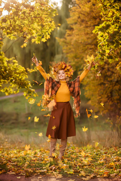 Пожилая женщина ходит по осеннему лесу. Бросает желтые листья вверх. - Фото, изображение