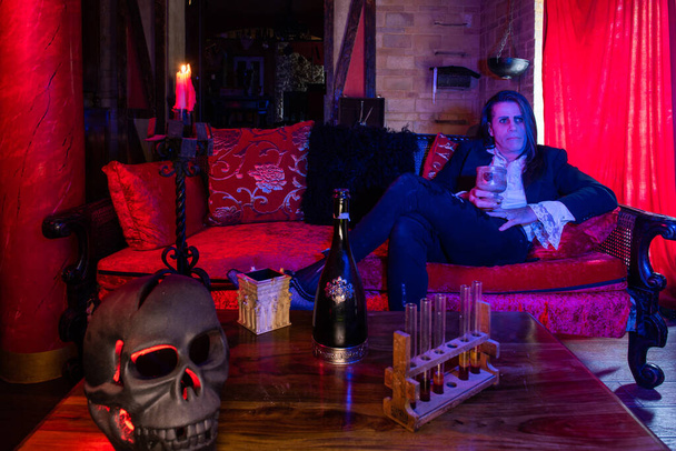 A disturbing man sitting on a red sofa in a Gothic-medieval setting - Foto, imagen