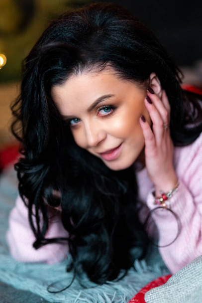 New Year photo session with festive decorations. Cheerful young woman in pink sweater posing to camera with dreamy face. Holidays concept - Photo, Image