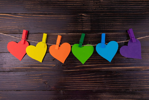 Hearts in rainbow colors hang on clothespins in a row on a dark wooden background. LGBT symbol.  - Фото, изображение