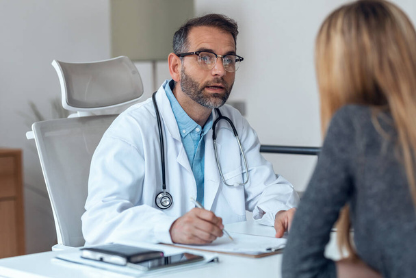 Shot of handsome mature male doctor talking while explaining medical treatment to patient in the consultation. - Foto, afbeelding