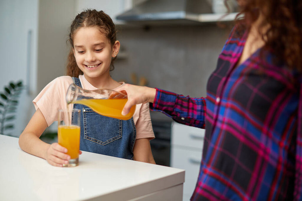 mamá vierte su bonita hija jugo de naranja para el desayuno - Foto, imagen
