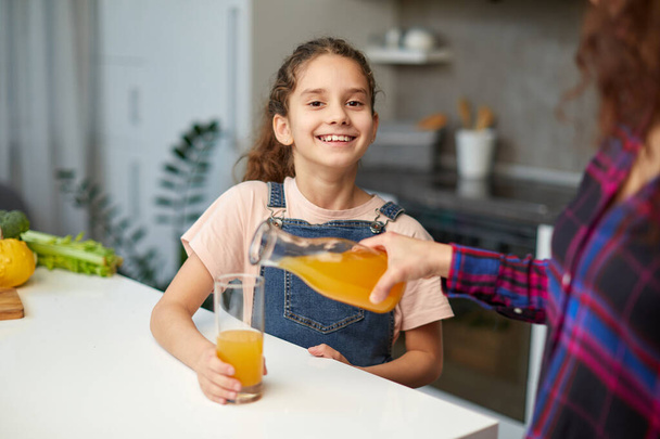 Portrait of a mom pours her cute daughter orange juice for breakfast - Fotografie, Obrázek