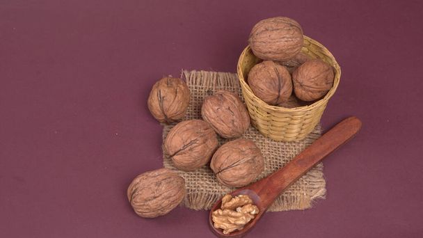Pile of walnuts with wooden spoon on purple background  - Fotoğraf, Görsel