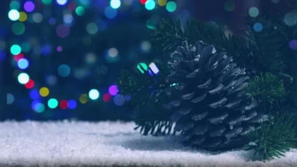 Cono de abeto sobre nieve blanca aislado sobre borroso árbol de Navidad luces fondo. - Imágenes, Vídeo