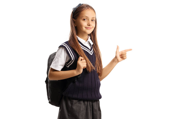 Schoolgirl with a backpack and a uniform pointing to the side isolated on white background - Foto, imagen