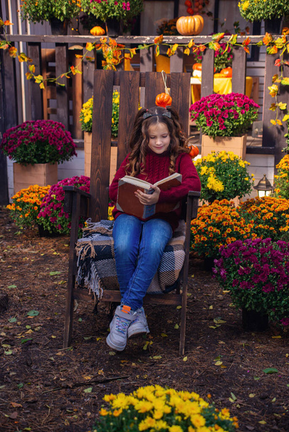 klein schattig meisje het lezen van een boek in de tuin in de herfst - Foto, afbeelding