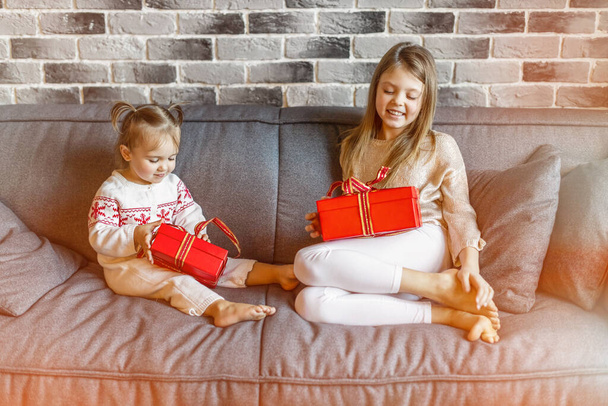 Two happy little sister girls with Christmas gifts on the couch smiling. Christmas concept. - Foto, Imagen