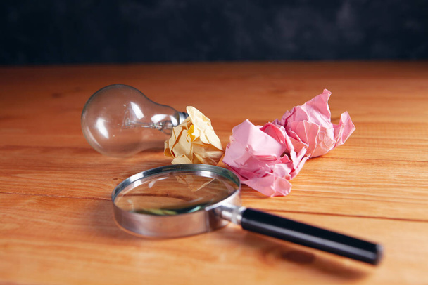 crumpled papers, magnifier and light bulb on the table - Foto, Imagen