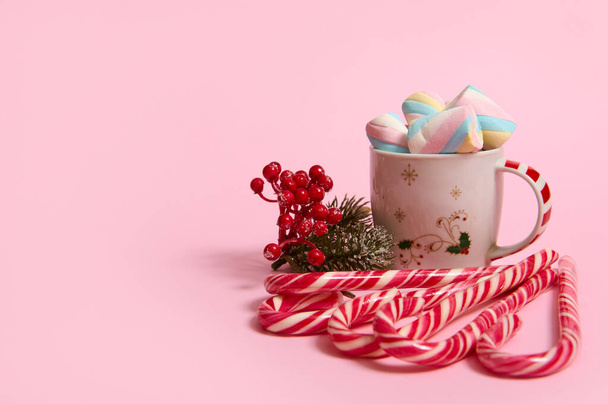 Beautiful minimalist Christmas composition with hot chocolate drink decorated with marshmallows and striped lollipops, candy canes isolated over pink colored backgroud with copy space for advertising - Foto, afbeelding
