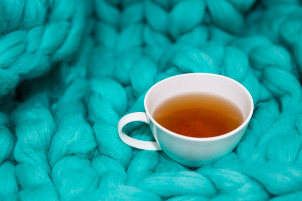 El concepto de comodidad y comodidad es una manta de punto verde en la que hay una taza de té blanco. Primer plano - Foto, imagen